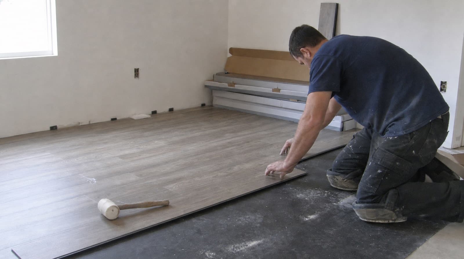 Flooring installer kneeling to fit vinyl plank flooring in an empty new-construction room