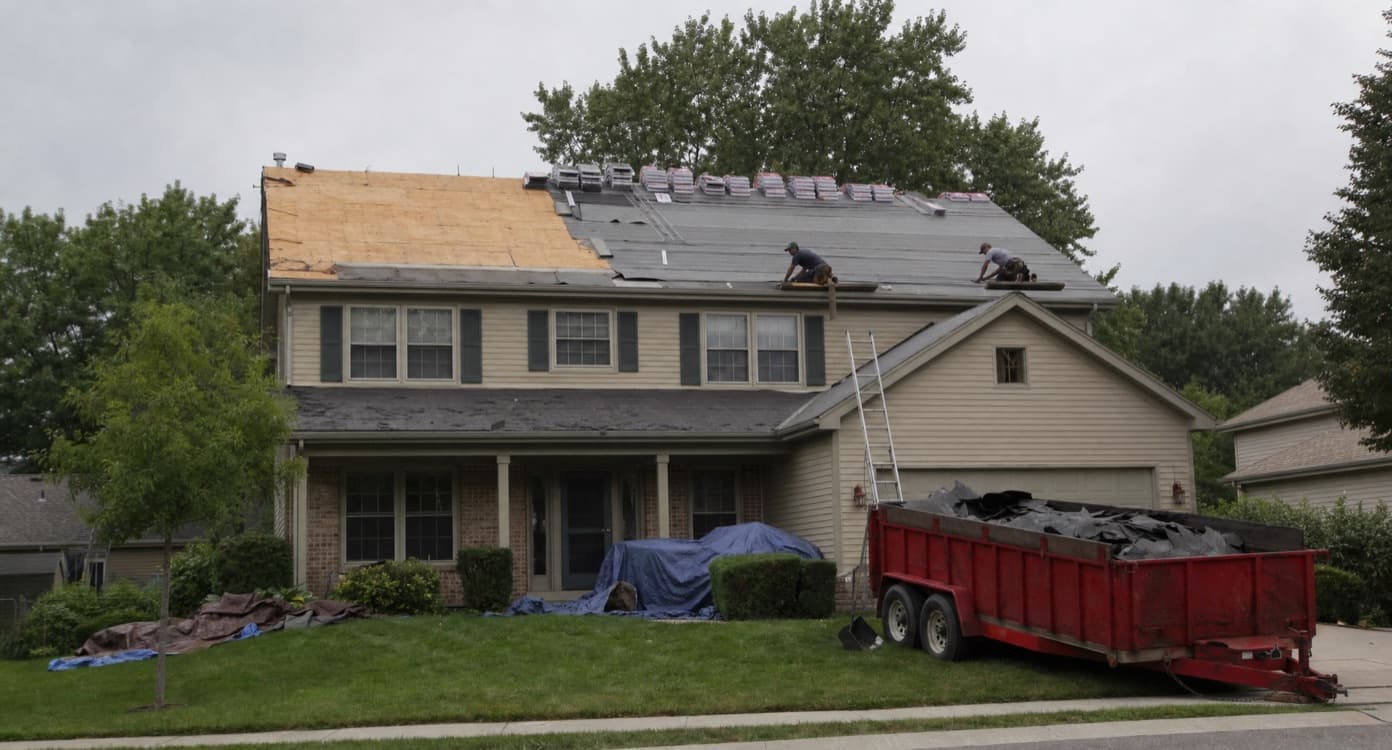 Roofing crew tearing off and re-decking the roof of a two-story house