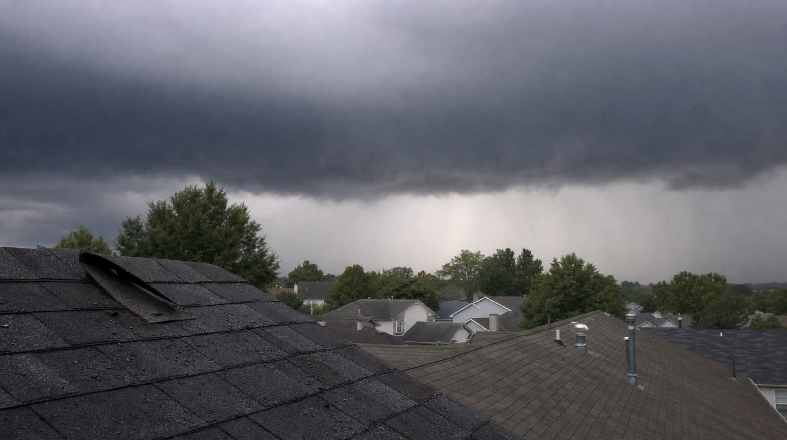 A storm front rolling in over a neighborhood of shingled rooftops